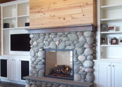 gas fireplace in living room with large round stone surround and wood mantel