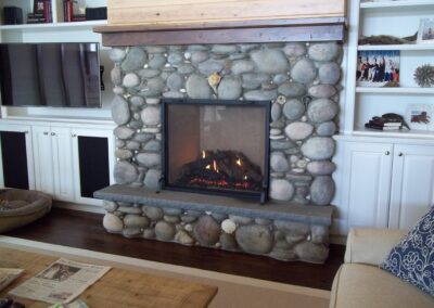 gas fireplace with large round stone surround and wooden mantel
